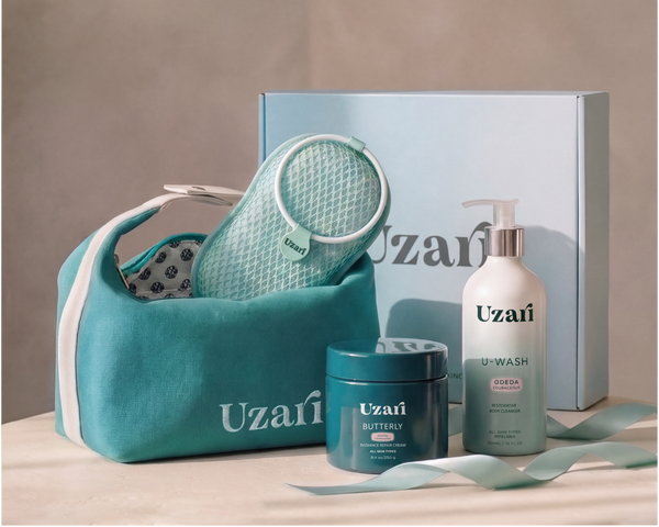 Uzaï skincare gift set featuring a teal mesh bath sponge in a matching teal zippered pouch, a white pump bottle of body wash, a teal jar of body cream, and a light blue gift box on a beige surface against a neutral background.