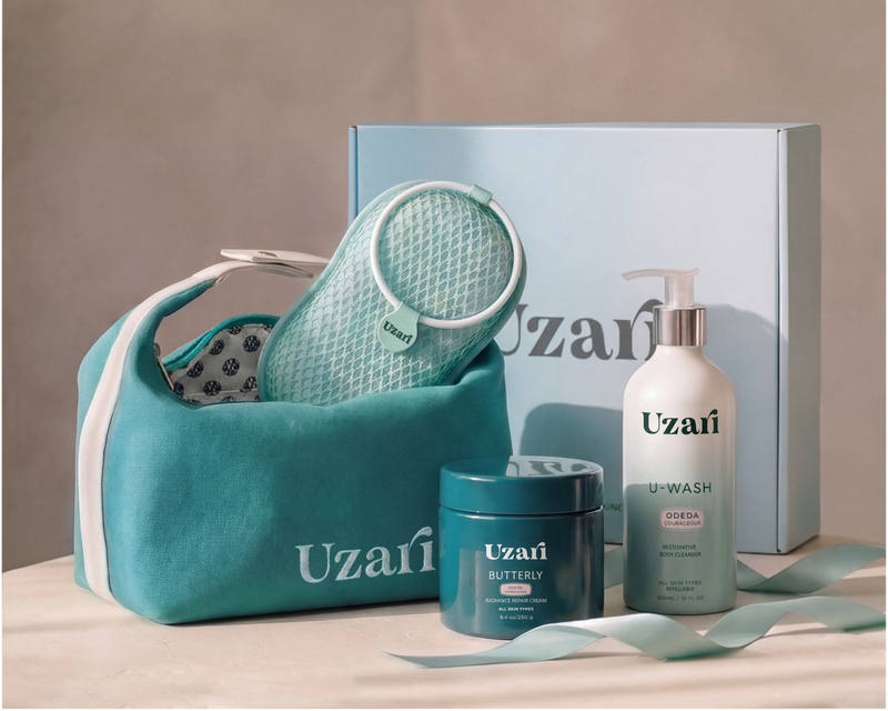 Uzaï skincare gift set featuring a teal mesh bath sponge in a matching teal zippered pouch, a white pump bottle of body wash, a teal jar of body cream, and a light blue gift box on a beige surface against a neutral background.