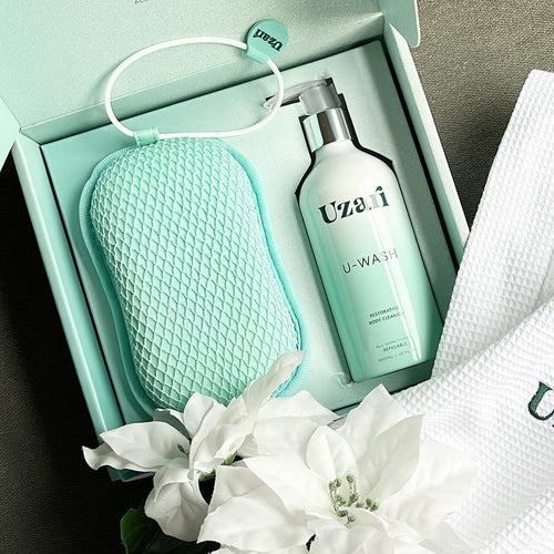 Uzai skincare product set with bottle, pouch, and towel on a gray surface with white flowers.